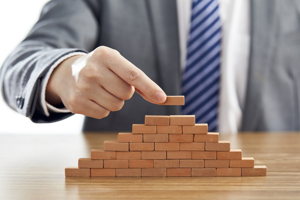 Businessman in a suit putting the last piece of a pyramid using wooden blocks - success concept